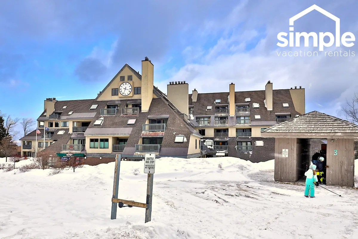This image features a snow-covered ground leading up to a striking building with a clock tower and an inviting entryway. The architecture reflects a classic resort feel, and the winter ambiance immediately connects to the ski resort proximity. Families and groups can be imagined gathering outside, with snow activities and après-ski mingling taking place.