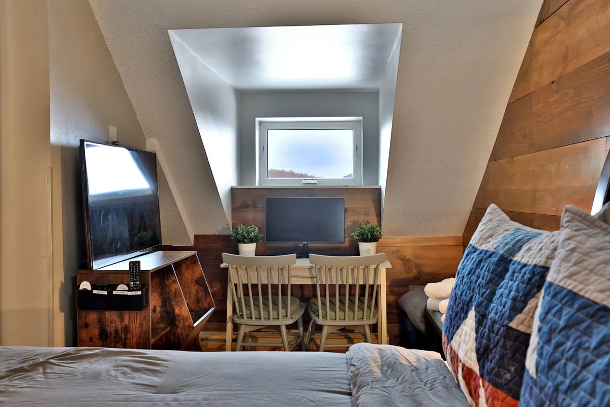 A cozy nook with a desk set beside a window, a plush bed, and a television, creating a perfect spot for remote work, reading, or watching TV. Sunlight streams in, enhancing the welcoming feel.