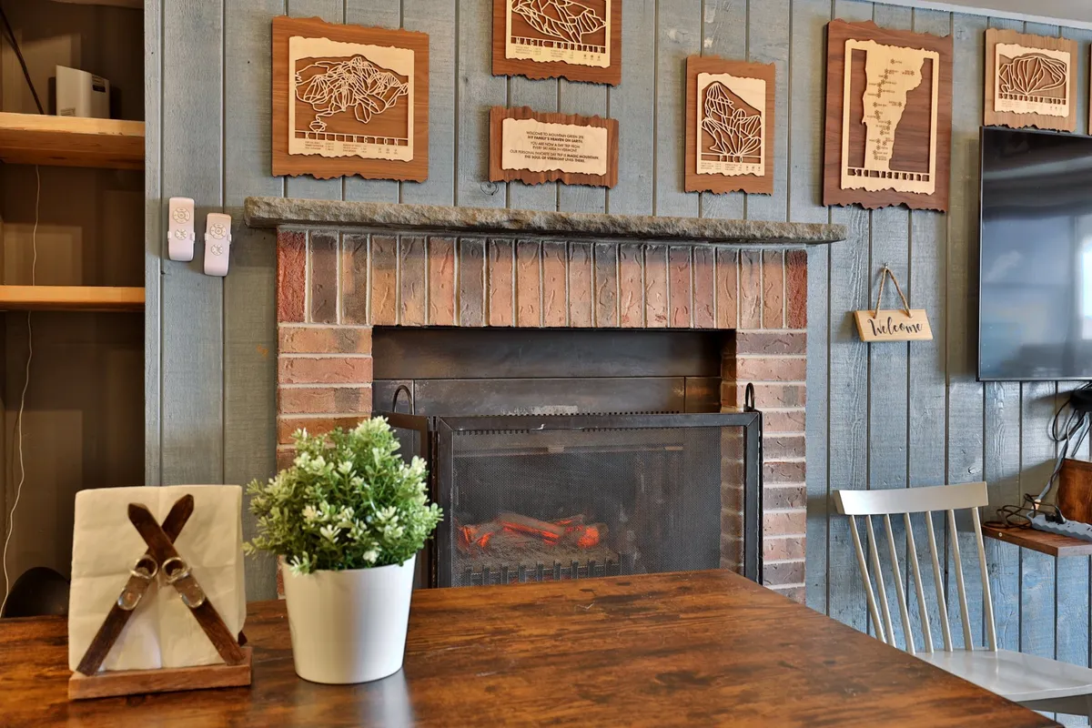 Features a cozy interior space with a fireplace, wooden wall art, and a table centerpiece—an inviting setting for gathering, sharing stories, or enjoying a meal and drinks after a day on the slopes.