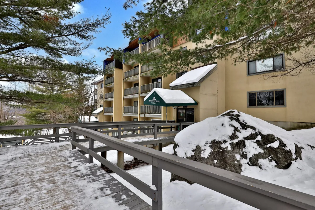 The exterior entrance to the property, featuring an entrance awning, a snow-covered rock, a wooden walkway, and balconies. While it shows a winter scene, the setup draws attention to the building’s inviting outdoor amenities and communal outdoor areas such as balconies and fire pit.