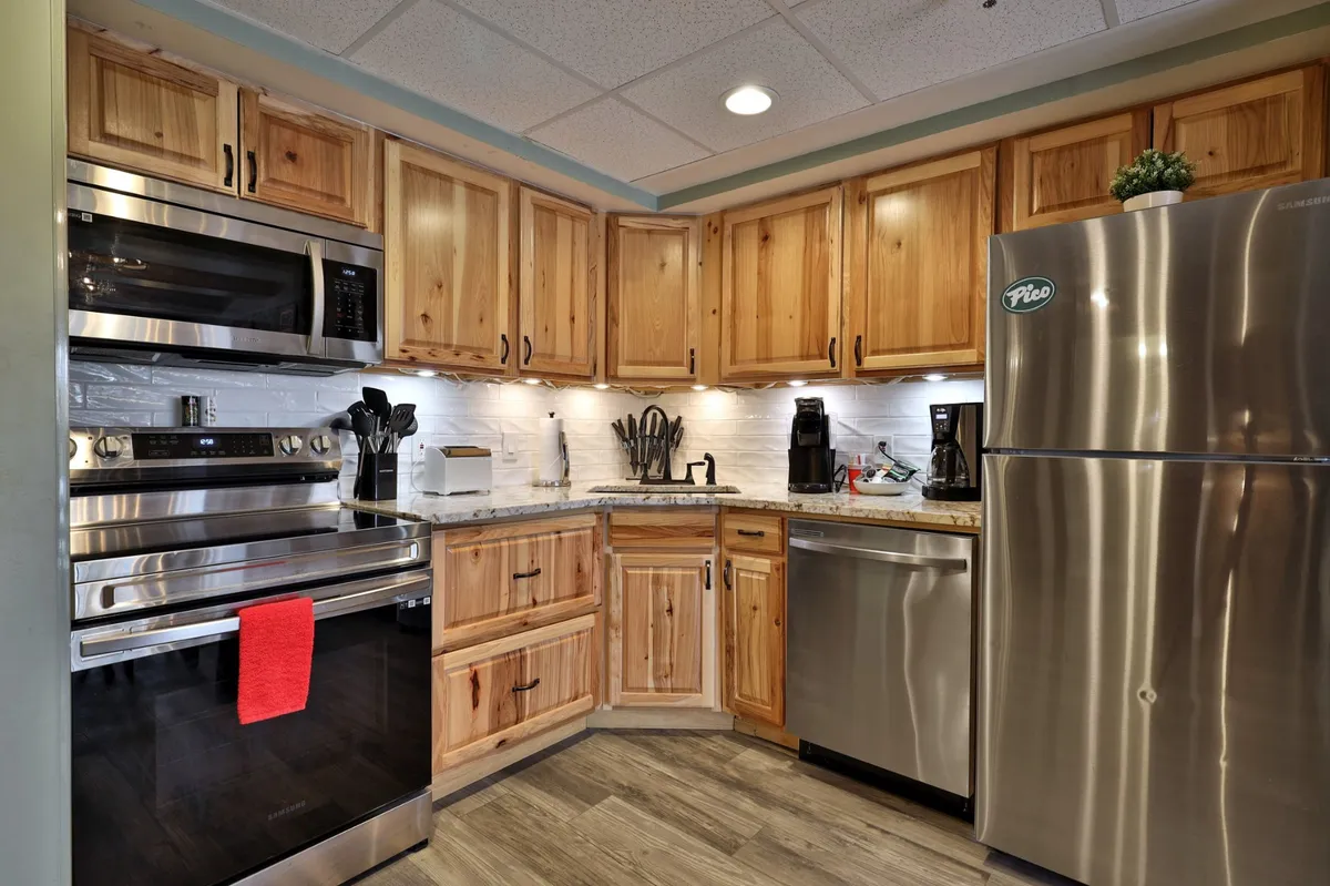 A view of a kitchen with stainless steel appliances, wooden cabinetry, and a granite countertop. The space feels open and ready for meal preparation or entertaining guests.