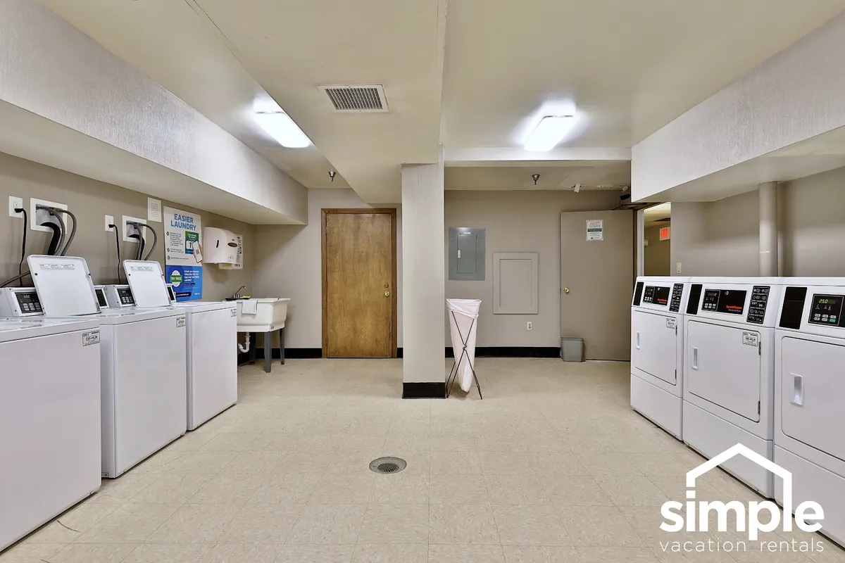 The image shows a practical, well-lit laundry room with rows of washing machines, dryers, and a utility sink. The clean, organized setup conveys efficiency and accessibility for guests looking to freshen their gear during their stay.